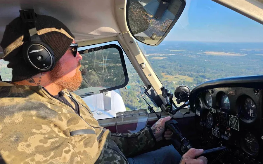 Anthony, a veteran, at the controls of Piper Cherokee N3480K during a VA Ready sponsored discovery flight, wearing a headset, beanie and sunglasses, with the Georgia landscape below